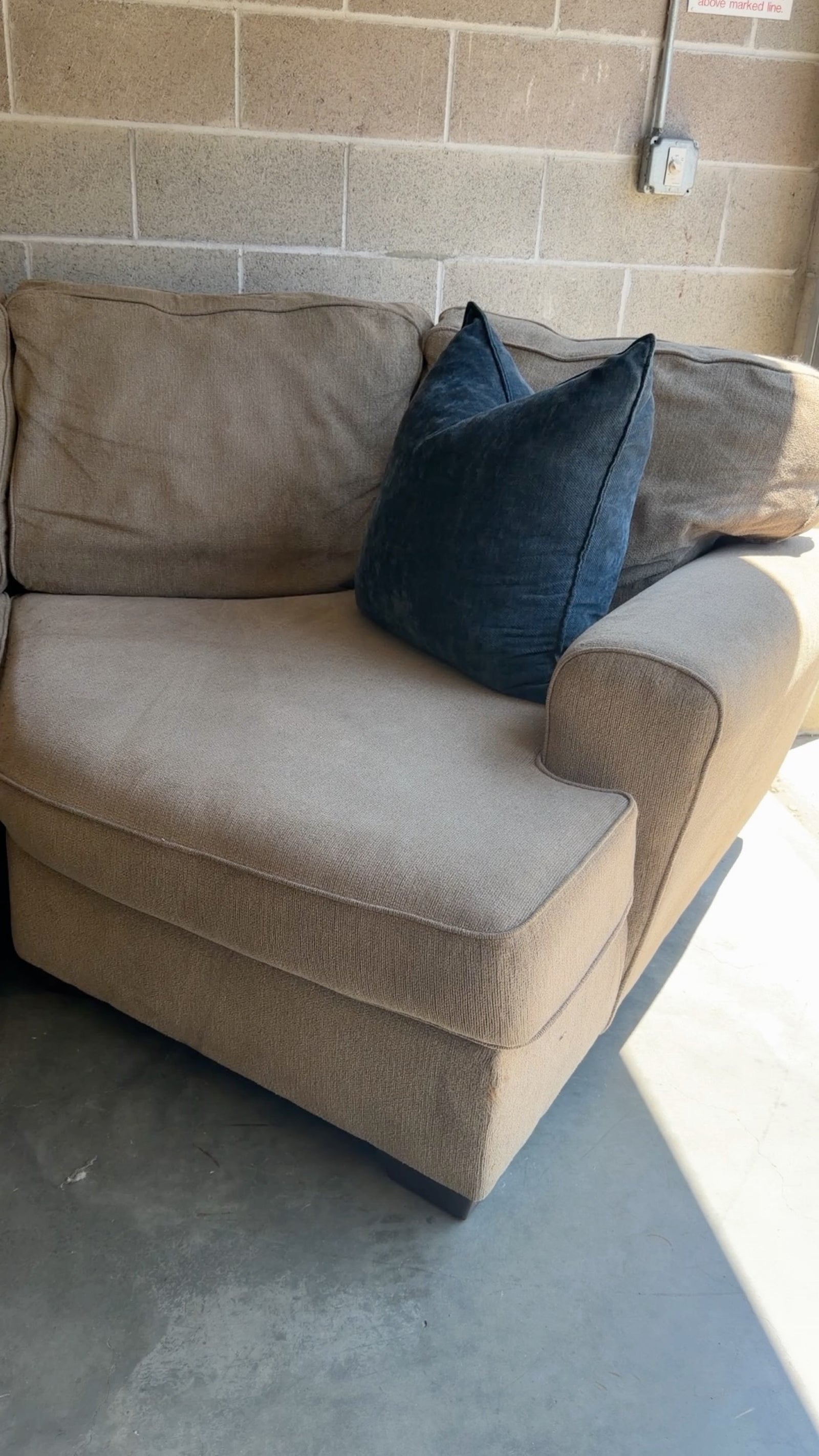 Tan fabric sectional sofa, close-up of the armrest showing a small tear in the fabric