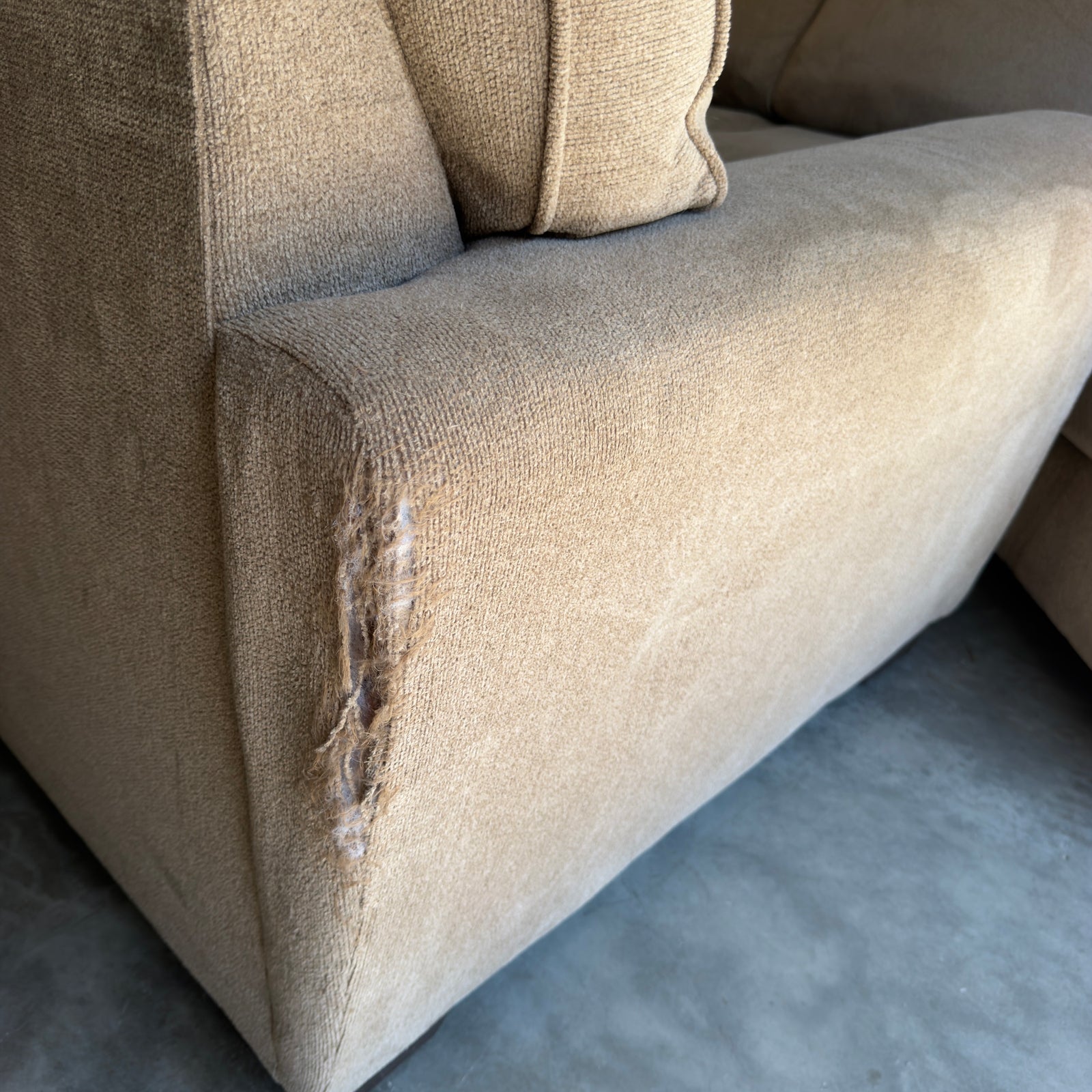 Tan fabric sectional sofa, close-up of the armrest tear from a different angle
